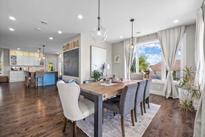 A spacious dining area with a wooden table and chairs, a kitchen in the background, and a large window with curtains. - Waterfront Home: Slide & Hot Tub (New Glasgow)