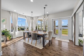 A dining area with a wooden table, chairs, and a view of a lake through large windows. - Waterfront Home: Slide & Hot Tub (New Glasgow)