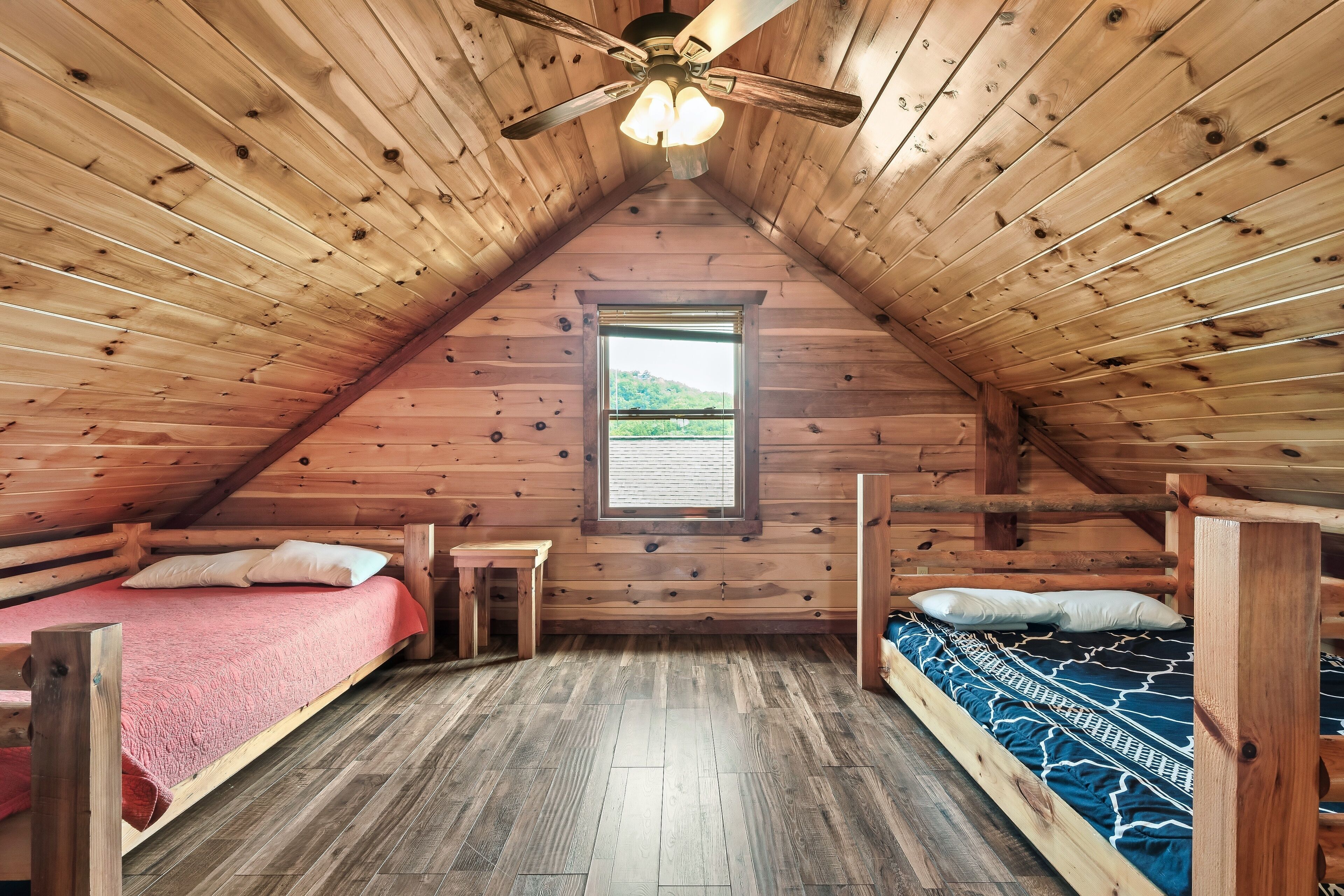 Una baita di legno con due letti a castello, una ventola a soffitto e una finestra vista verde.