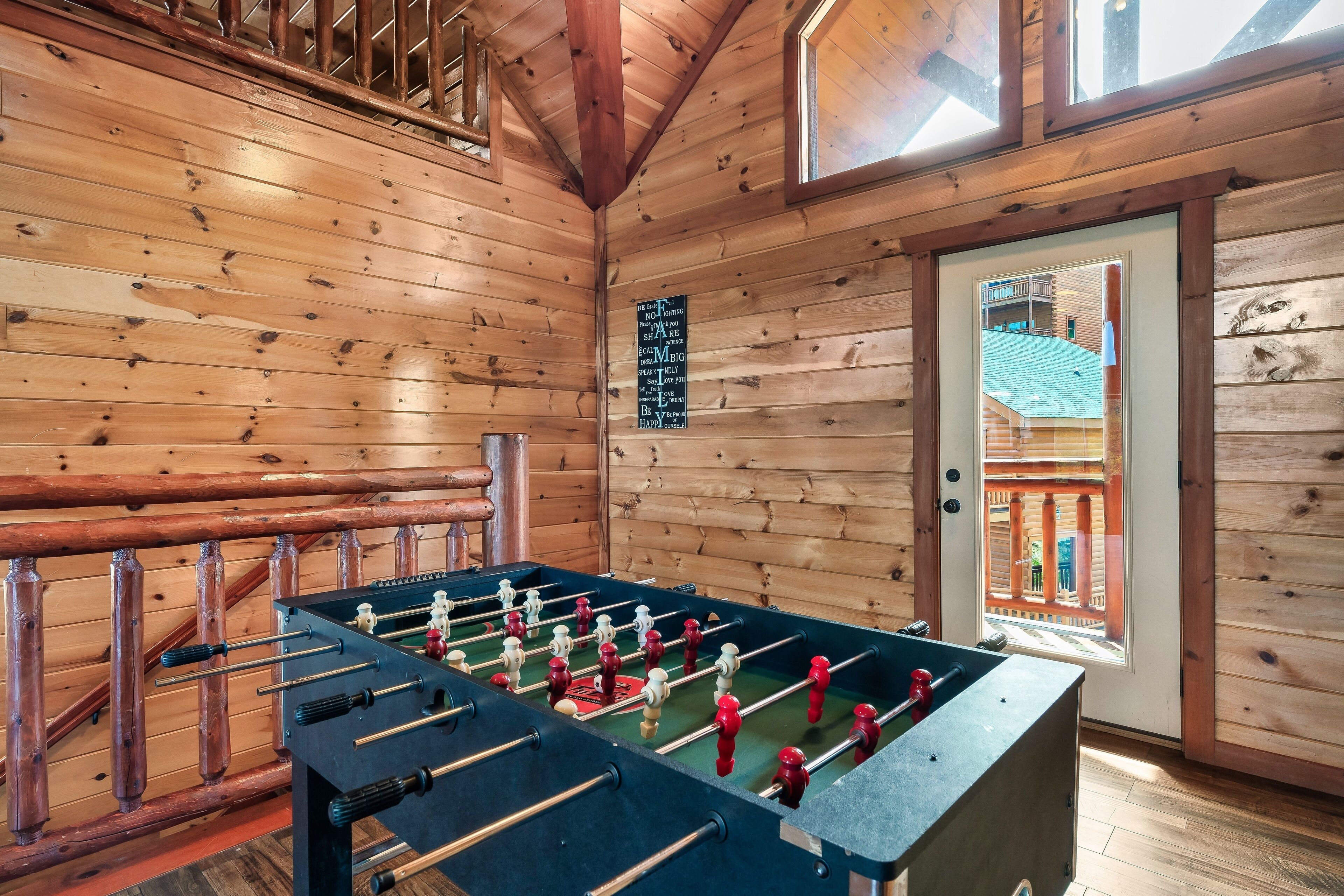 A wooden-floored room with a foosball table, a window, and a door leading outside.