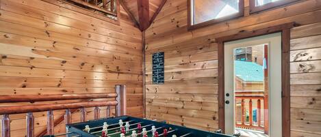 A wooden-floored room with a foosball table, a window, and a door leading outside.