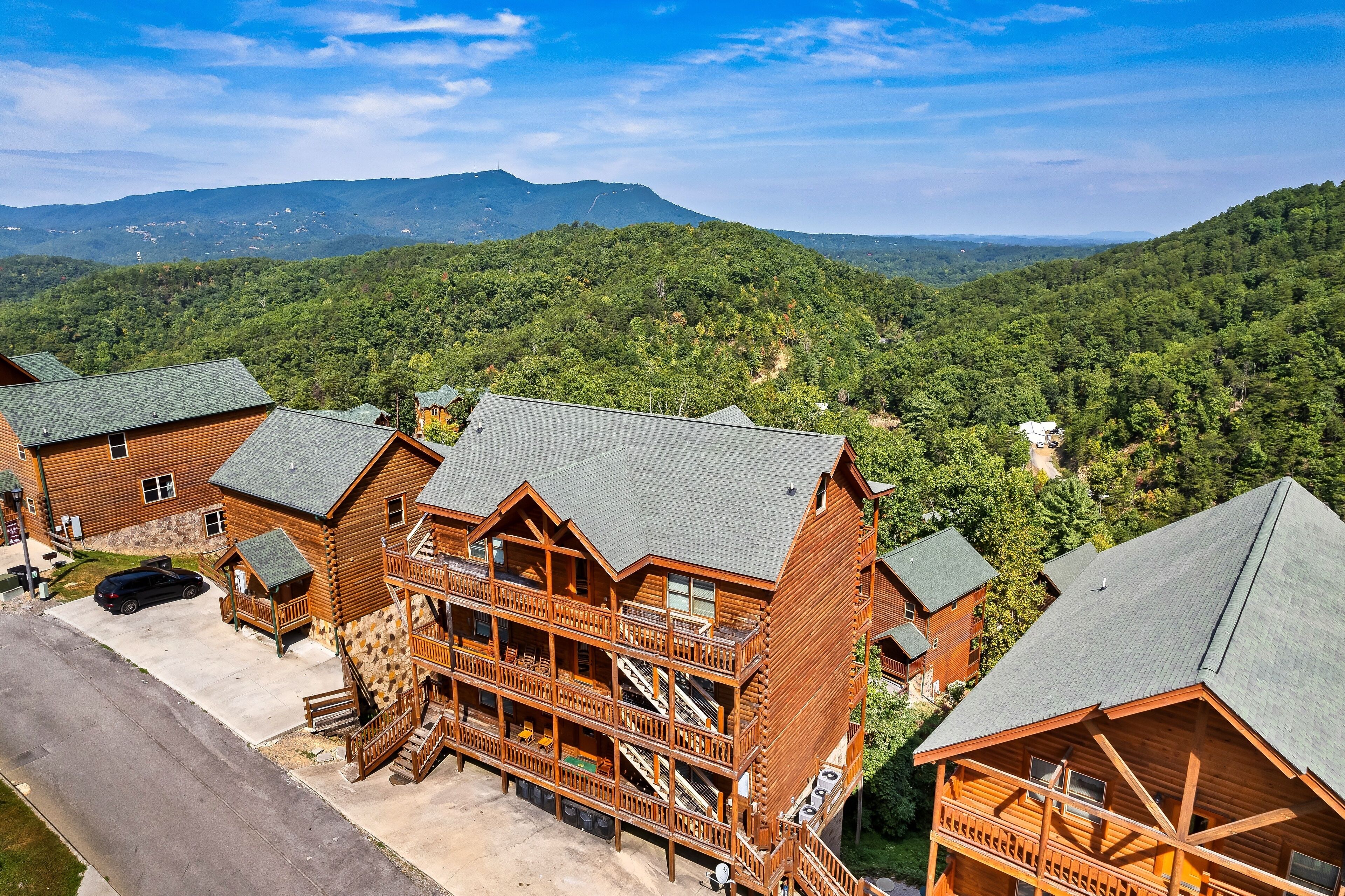 Un hotel tipo cabaña de troncos de varios pisos, con una escalera central, rodeado de un bosque frondoso y montañas al fondo.