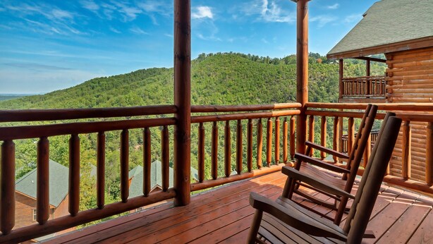 Una terraza de madera con una silla de madera, con vista a una ladera boscosa.
