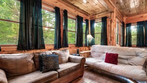 A wooden cabin interior with two sofas, a lamp, and large windows with curtains. - Grand Mountain Retreat w/ Games & Hot Tub (Pigeon Forge)