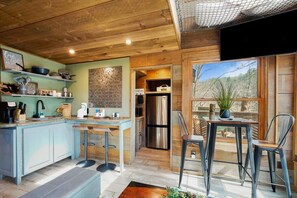 A modern kitchen with a wooden ceiling, a brick wall, and a large window with a view of trees. - Rustic Wooded Escape w/ Hot Tub and Views (Sevierville)