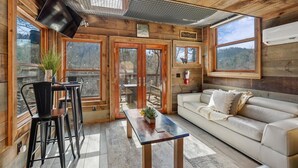 A wooden cabin interior with a sofa, dining table, chairs, and a TV. - Rustic Wooded Escape w/ Hot Tub and Views (Sevierville)