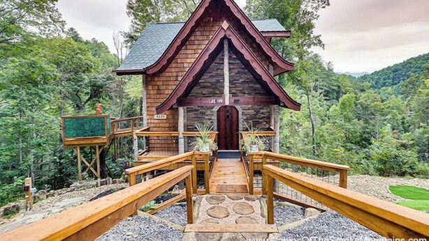 A wooden cabin with a steep roof, a front door, and a small porch area with railings. - Rustic Wooded Escape w/ Hot Tub and Views (Sevierville)