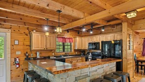 Una cucina in legno dallo stile chalet con un'isola in pietra, sgabelli da bar ed elettrodomestici moderni.