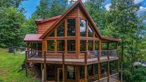 Useista kerroksista koostuva puinen mökki, jossa on punainen katto, suuret ikkunat ja parveke.