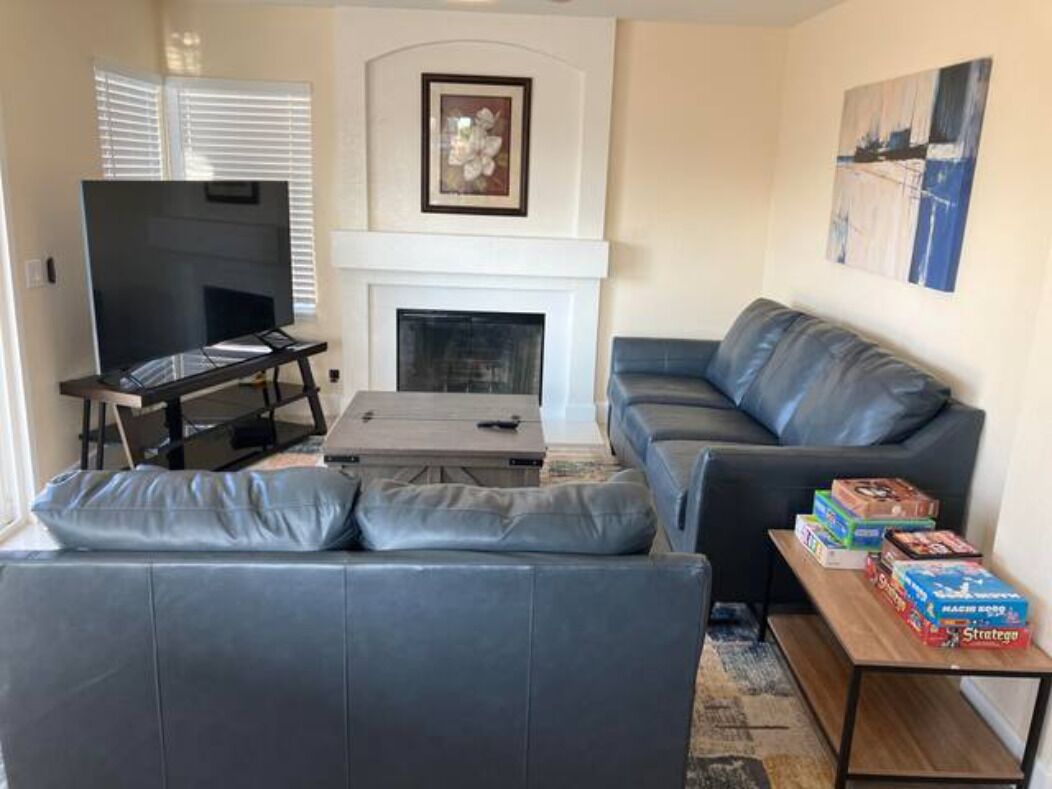A living room with a grey sofa, a coffee table, a flat-screen TV, a fireplace, and a painting on the wall.