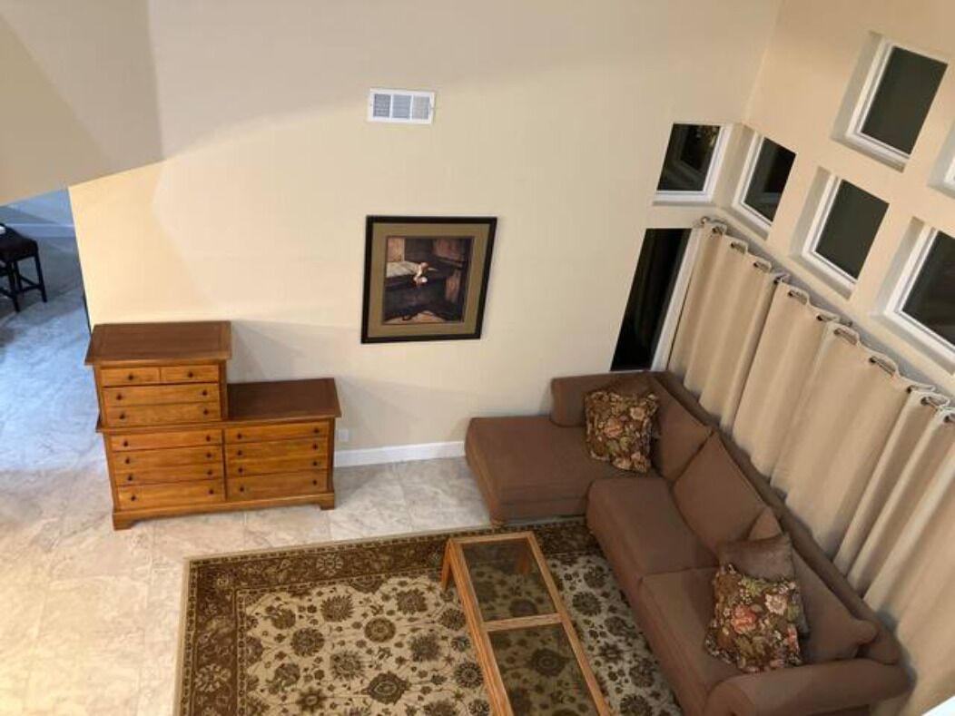 A living room with a brown sofa, a wooden dresser, a patterned rug, and a framed picture on the wall.
