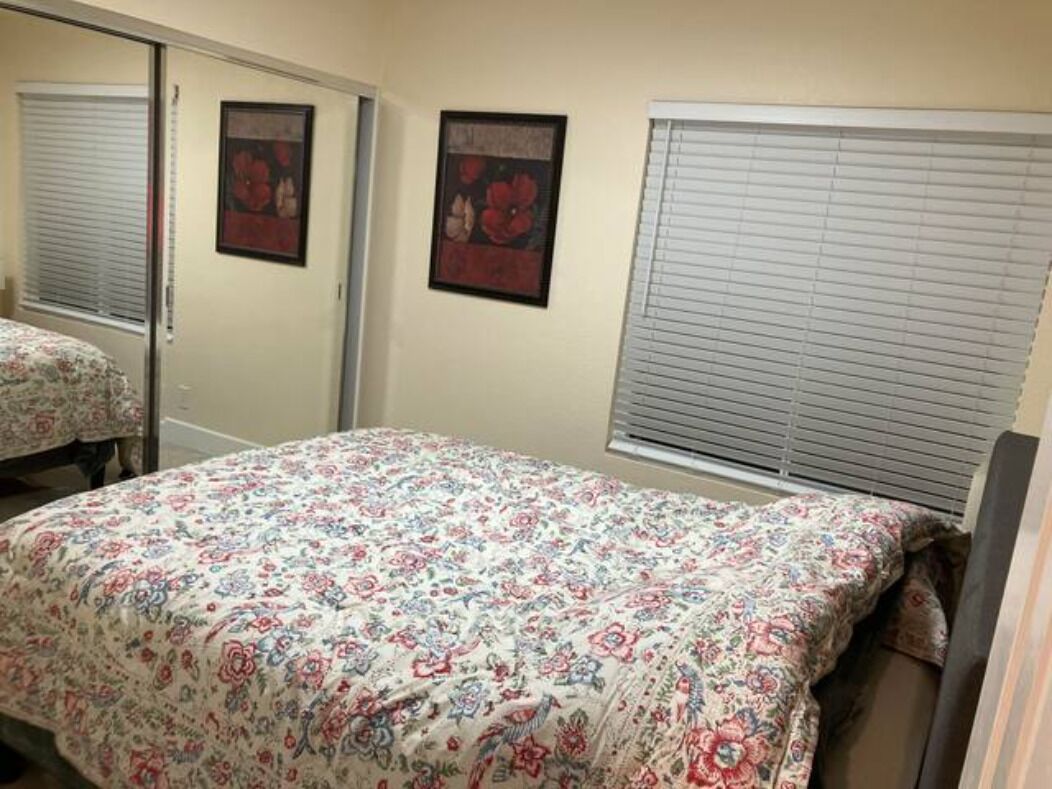 A bedroom with a floral bedspread, a large mirror, and two framed pictures on the wall.