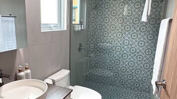 A bathroom with a round sink, toilet, and shower.