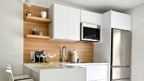 Eine moderne Küche mit weißen Schränken, einem Edelstahl-Kühlschrank und einer kleinen Kochinsel mit Spüle und Barhocker.
