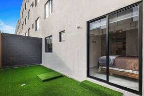 A modern room with a large sliding glass door, a bed with a wooden frame, and a small window. - Modern Apartment with Pool in Querétaro (El Marques)
