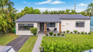 Une maison moderne à deux étages, avec un toit recouvert de tuiles grises, de grandes fenêtres et un petit patio aménagé avec du mobilier d’extérieur.