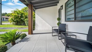 Un espace extérieur aménagé, abrité et doté d’un design moderne, comprenant un banc et une table, et offrant une vue sur la rue et la verdure en arrière-plan.