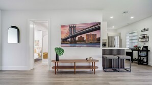 Un salon moderne avec un grand tableau représentant un pont, une console en bois et un coin salon avec une petite table et des chaises.