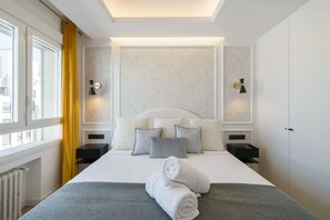 Ett modernt hotellrum med en stor säng, två sängbord, ett litet bord, ett element och ett fönster med gardiner.