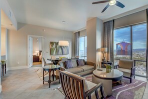 Ein modernes Hotelzimmer mit großem Fenster und Blick auf die Stadt, einer Couch, einem Essbereich und einem Deckenventilator.