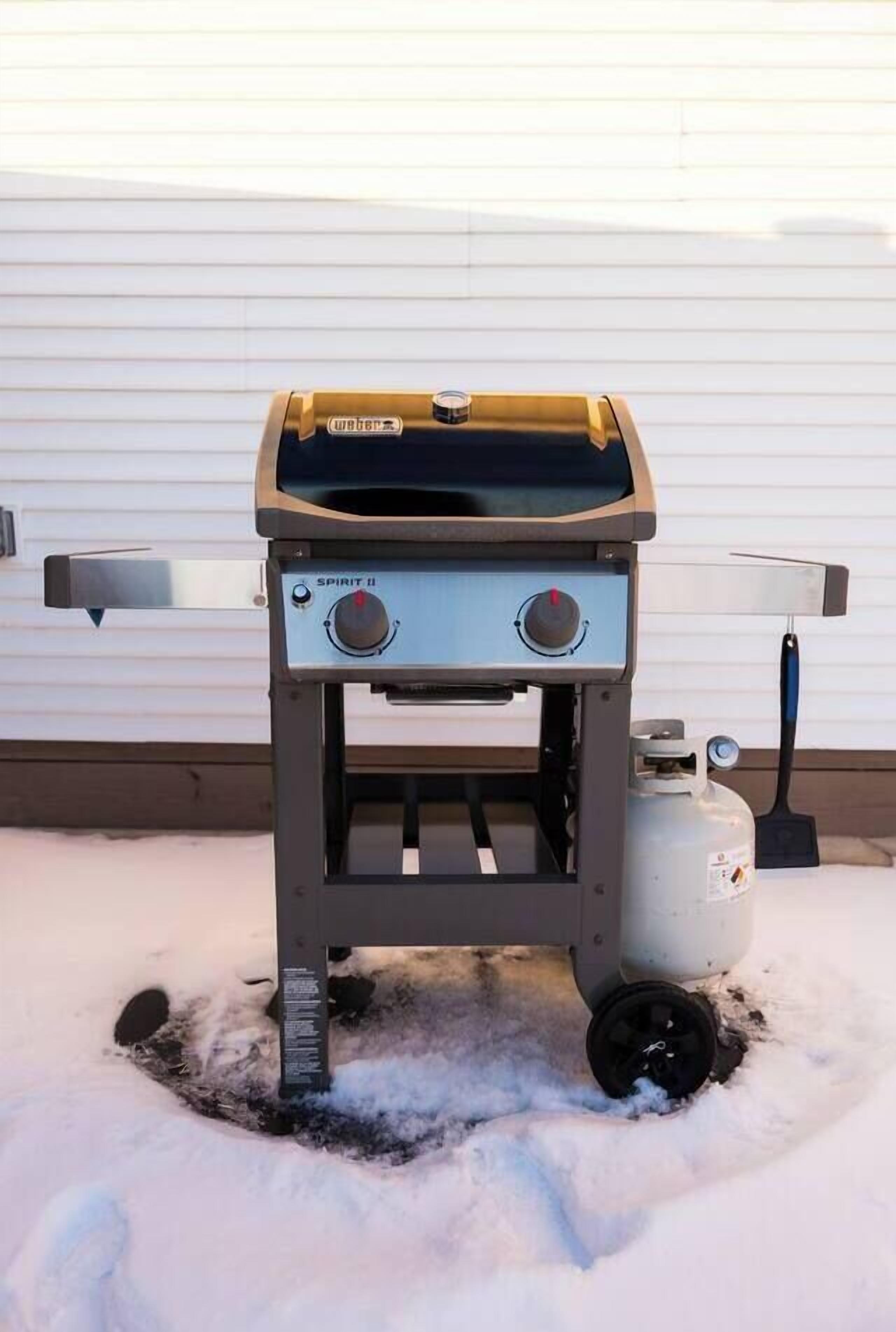 Un barbecue portable doté de deux boutons de réglage, d’une bouteille de propane et d’un manche noir.