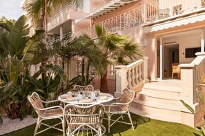 Eine Terrasse mit einem runden Esstisch, umgeben von Korbstühlen, und einer Treppe, die zu einer oberen Ebene führt.