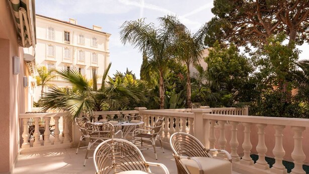 A terrace with wicker furniture, a round table, and a view of a building with balconies. - Carla Rosa 5 Apartement Terrazza - 2 BDR Piscine (Cannes)