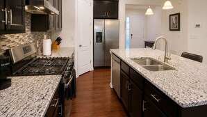 A modern kitchen with dark cabinetry, a stainless steel refrigerator, a granite countertop, and a built-in dishwasher. - 5B4B in Parker w/ Game Room, Fenced Yard & Garage (Parker)