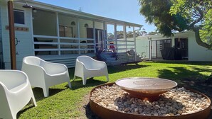 A covered outdoor seating area with white plastic chairs and a circular stone fire pit. - Bendy Beach House, beach side property at Washerwomans beach and Sting Ray Bay (Bendalong)