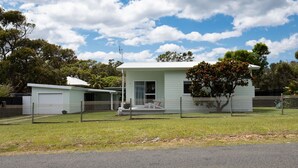 A single-story house with a fenced yard, a covered porch, and a large tree in front. - Bendy Beach House, beach side property at Washerwomans beach and Sting Ray Bay (Bendalong)