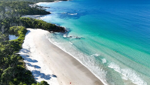 A beach with clear turquoise waters and white sand, surrounded by dense green vegetation. - Pippis Cottage, bringing back the charm of the iconic old Bendalong School House (Bendalong)