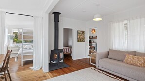 A modern living room with a fireplace, wooden flooring, a sofa, and a dining area with a table and chairs. - Pippis Cottage, bringing back the charm of the iconic old Bendalong School House (Bendalong)