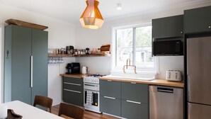 A modern kitchen with grey cabinets, a wooden countertop, a gas stove, a dishwasher, and a window with a view of the outdoors. - Pippis Cottage, bringing back the charm of the iconic old Bendalong School House (Bendalong)