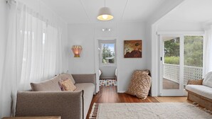 A spacious living room with a sofa, a patterned rug, and a view through a glass door to the outdoors. - Pippis Cottage, bringing back the charm of the iconic old Bendalong School House (Bendalong)