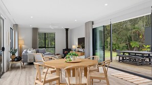 A modern living room with a fireplace, a dining area, and a large sliding glass door leading to a deck. - The Bird House Manyana (Manyana)