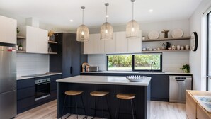 A modern kitchen with a central island, pendant lights, and a view of greenery outside. - The Bird House Manyana (Manyana)