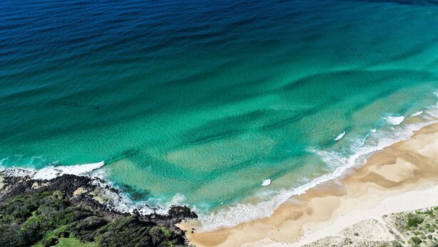 An aerial view of a beach with clear turquoise waters, sandy shore, and rocky outcrops. - The Bird House Manyana (Manyana)