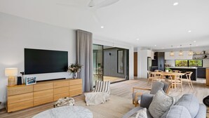 A modern living room with a flat-screen TV, a wooden entertainment unit, and a dining area with a table and chairs. - The Bird House Manyana (Manyana)