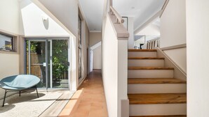 Un interior moderno con una escalera, un puerta de cristal que da a un jardín y una silla junto a la puerta.