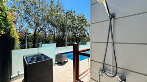 Et moderne badeværelse med bruser, pool med glasvægge og udsigt over et poolområde med træer.
