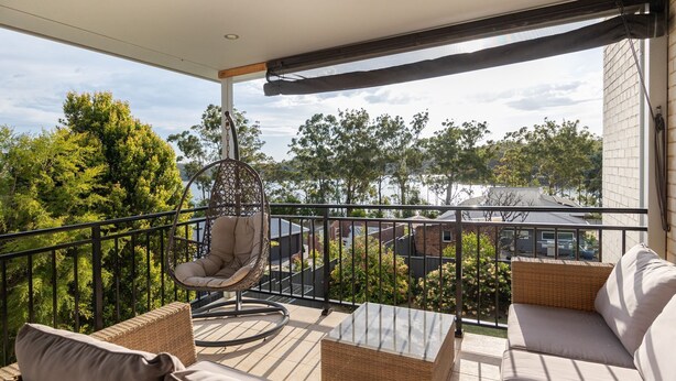 Un balcon avec un fauteuil suspendu, un canapé et une table en verre.