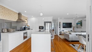 Une cuisine moderne avec des meubles blancs, un îlot central et un coin repas comprenant un canapé gris et un téléviseur.