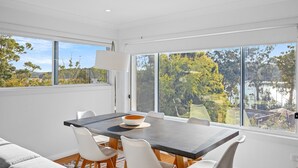 Un espace de restauration moderne, doté d’une grande table, de chaises blanches et offrant une vue sur les arbres et les bâtiments grâce à de larges fenêtres.