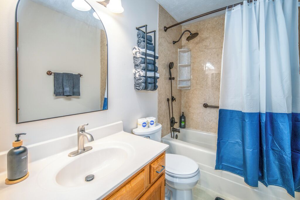 Un baño con un lavamanos blanco, inodoro, ducha y cortina de ducha azul y blanca.