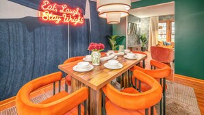 A dining area with a neon sign, orange chairs, and a wooden table set for four. - Wright Stay: Hot Tub, Game Room, Sunroom, Fire-Pit (Dayton)