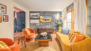 A modern living room with a sofa, armchairs, a coffee table, and artwork on the walls. - Wright Stay: Hot Tub, Game Room, Sunroom, Fire-Pit (Dayton)