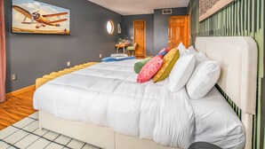 A bedroom with a large bed, a painting of an airplane on the wall, a wooden floor, and a green-striped wall. - Wright Stay: Hot Tub, Game Room, Sunroom, Fire-Pit (Dayton)