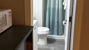 Un baño con inodoro, ducha y un microondas en la encimera.