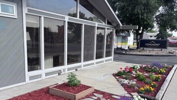 Un edificio con ventanas amplias, un cartel que dice 'LONGMONT' y un área ajardinada con macizos de flores.