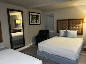 Ein Hotelzimmer mit einem großen Bett, einem Sessel, einem Spiegel und einem gerahmten Bild an der Wand.